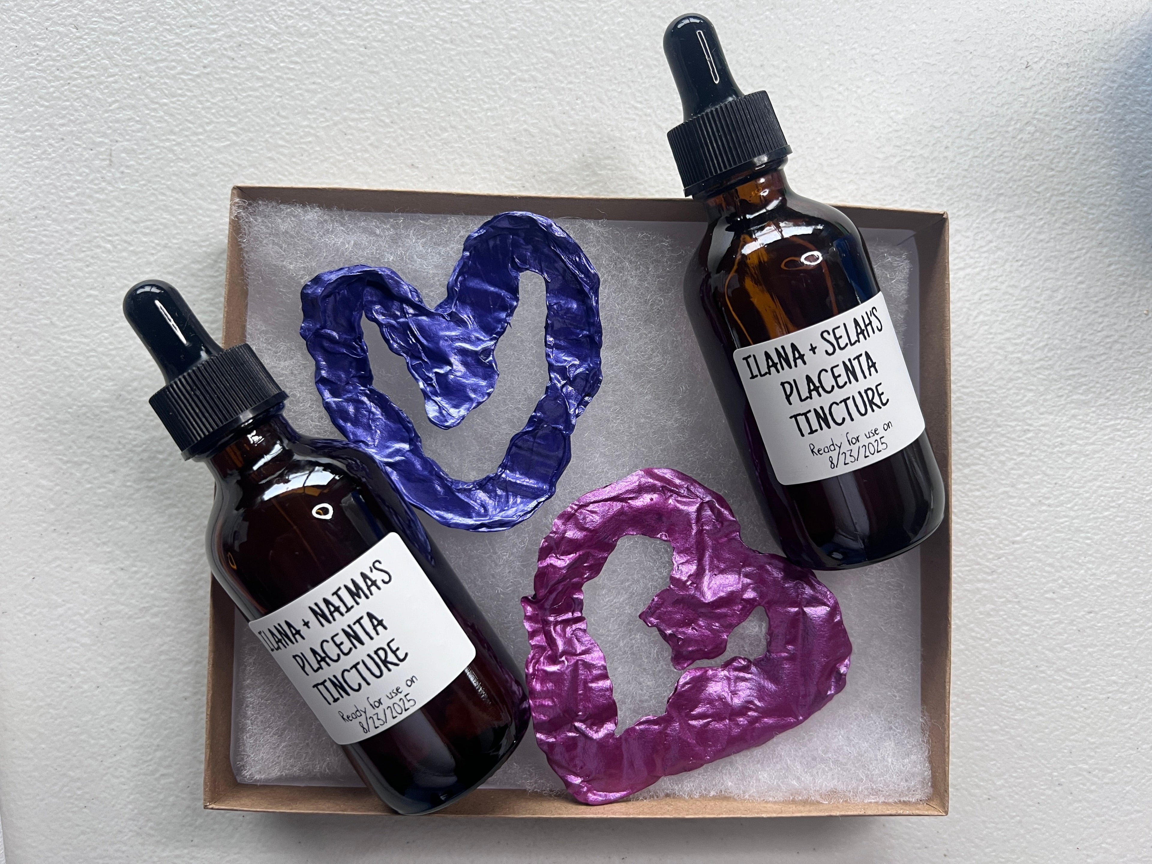 Two bottles of placenta tincture with decorative stones on a textured surface