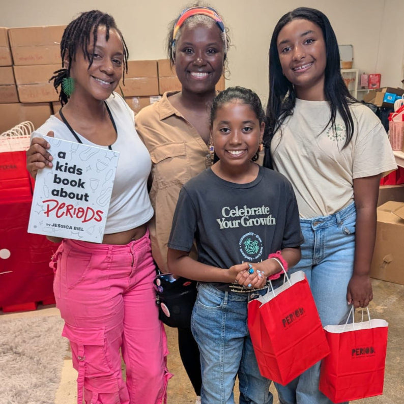 Two black women and two children, holding menstrual doula period products at their local Miami warehouse.